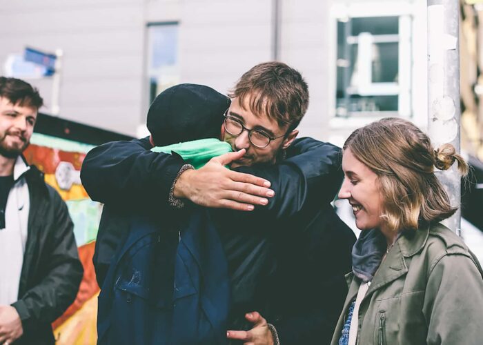 A group of people hugging in front of a mural.