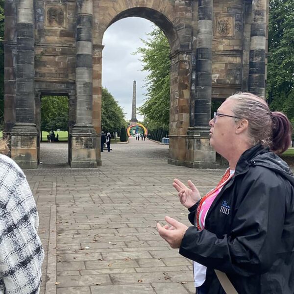 Two women talking in front of an arch in a park.