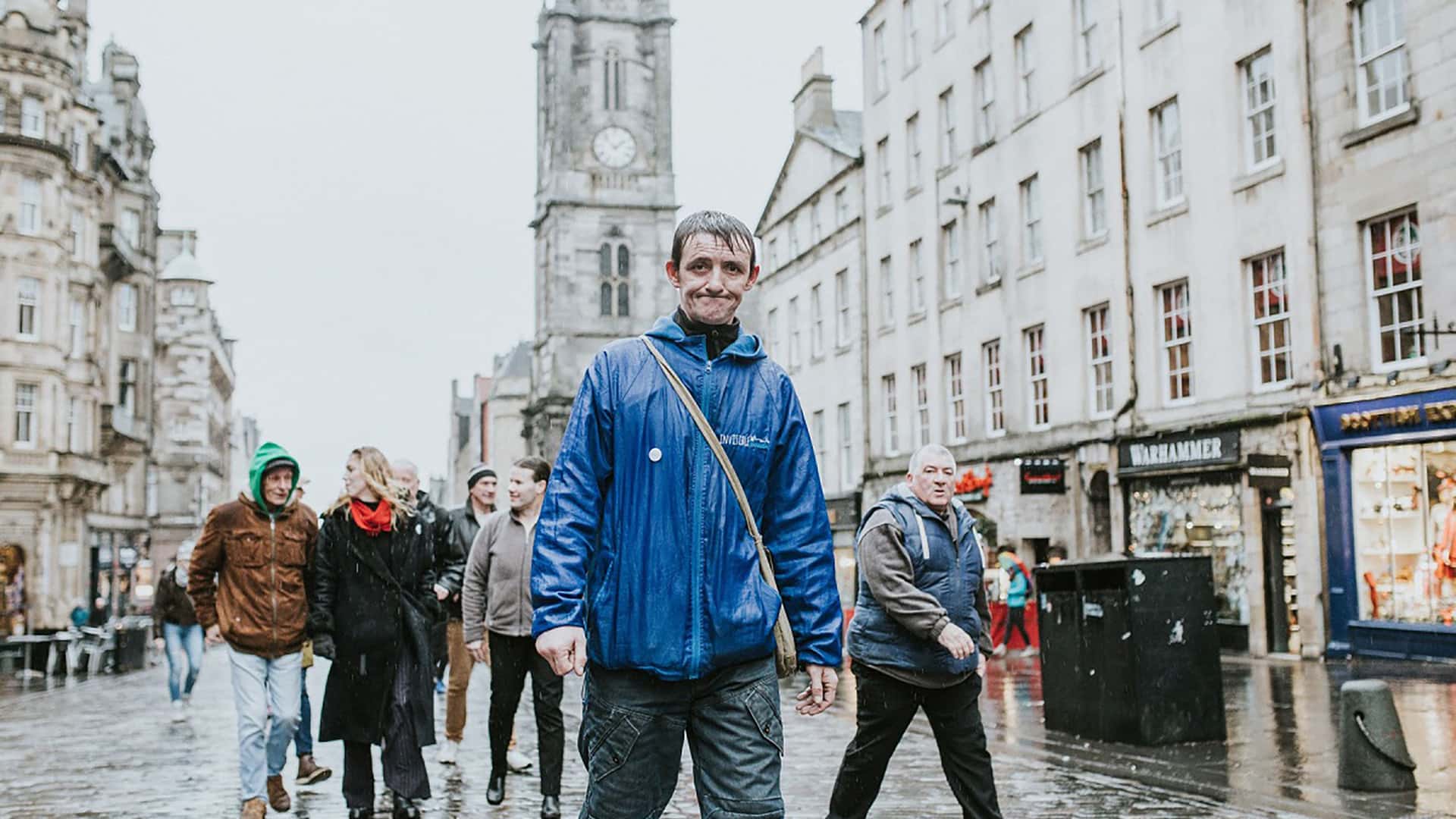 A man in a blue jacket walking down a street in edinburgh.
