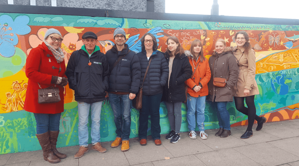 A group of people from Invisible Manchester standing in front of a colorful mural.