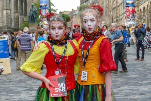Two women dressed up in clown costumes on a cobbled street in the UK.