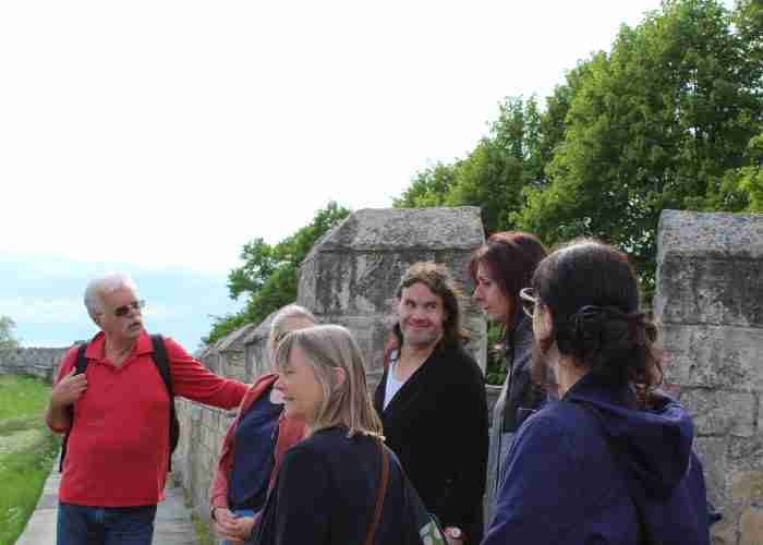 A group of people stands by a stone wall outdoors in York; an older man in a red shirt, likely a local tour guide, speaks as the others listen attentively—one of the top things to do in the city.