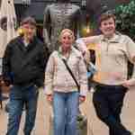 Three people stand in front of a bronze statue of a man in a courtyard, with fairy lights and a grey building in the background—a perfect scene often encountered on Northern Ireland Walking Tours.